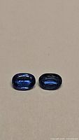 Pair of oval cut untreated cornflower blue kyanite gemstones displayed on a neutral background showing their size and color in natural light.
