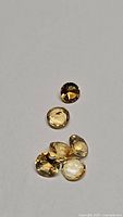 Photo showing seven natural golden citrine gemstones of similar size and round cut on a plain surface.