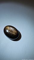 Photo of an opaque oval cabochon sapphire exhibiting golden sheen and flashes on a blue background.