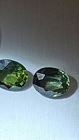 Two oval cut bright green sapphires on a white background under light