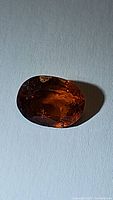 Close-up photo of a natural untreated hessonite garnet oval cut gemstone showing deep burnt orange color and internal clarity.
