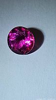 Close-up photo of round cut hot pink topaz gem showing vibrant color and faceting