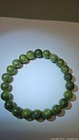 Photo showing circular arrangement of green jade beads forming a chunky bracelet on a white surface with clear bead details and natural color variation.