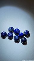 Photo of eight natural round cabochon Lapis Lazuli gemstones showing their deep blue color and gold pyrite flecks