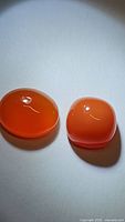 Close-up photo of two Mandarin orange carnelian cabochon gemstones on white background, showing their rich orange color and smooth polished surfaces.