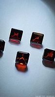 Photo showing five square emerald cut garnet gemstones with deep cherry red color, arranged closely to display facets and clarity.