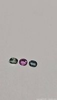 Three natural multicolored oval cut sapphires in greenish-gray, purple-pink, and bluish-gray.