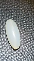 Photo showing the elongated oval shape and smooth, polished surface of the white moonstone cabochon placed on textured black background, highlighting its pearly translucency and cat's eye effect.