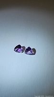 Two natural purple amethyst gemstones placed on a light surface photographed to show the color and cut.