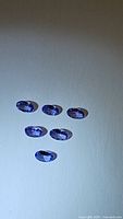Six oval cut blue purple tanzanite gemstones laid out on a light surface under lighting to show color and cut.