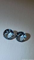 Pair of natural sky blue topaz gemstones placed side by side on white background, showing their round faceted cuts and transparent light blue color.
