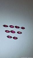 Top view of nine natural untreated marquis cut rubies laid out on white background showing shapes and color tones from red to pink.