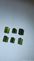 Photo of six rough polished AAA chrome tourmaline crystals with varying green shades on a white background.