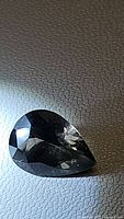 Close-up image of pear-shaped faceted gemstone showing facets and unique color in diffused light