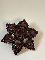 Front view of antique Victorian star-shaped brooch with garnet gemstones, showing one missing stone at outer cluster.