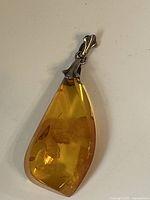 Close-up of front side of teardrop amber pendant with silver bail.