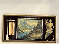 Full view of the framed artwork showing mountain cabin painting, thermometer on the left, and woman on horse cutout on the right.