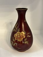 Front view of red lacquer vase showing gold floral design and smooth surface.