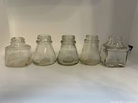 Side view of five clear glass antique inkwells in varied shapes, showing rust spots and wear.