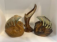 Three-piece lot of Van Briggle ceramic swan vases and an abstract vase arranged on a white shelf