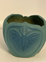 Front view showing butterfly relief on turquoise ceramic vase with wavy rim.