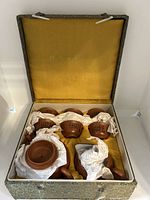 Full set of one clay teapot and six matching cups in original box with yellow fabric lining and protective tissue paper.