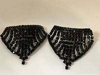 Front view of two black vintage Musi shoe clips with intricate beaded, scalloped triangular design and dangling bead fringe.