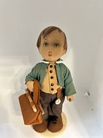 Full-length photo of the vintage porcelain doll showing clothing, suitcase, and base.