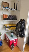 Wide view showing all items including lantern, cooler, stove, binoculars, flashlights, and backpack on shelves.