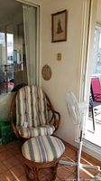 Wooden chair with striped upholstery and matching footrest beside Nordik standing fan and wall decorations.