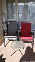 Two patio chairs side by side, one grey and one red, with a small square glass and metal table in front.