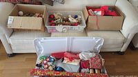 Boxes and container with assorted Christmas decorations and wrapping materials including ribbons, gift boxes, and rolls of wrapping paper