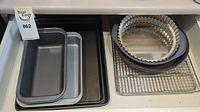 Metal baking pans of various sizes, cooling racks, and a round, fluted edge tart pan on a shelf.