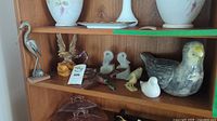 Shelf with various small decorative bird sculptures made of metal, wood, ceramic, and glass including a large ceramic bird and smaller figurines