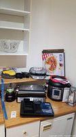 Overview of the kitchen counter showing all items in the lot placed for display, including boxed pizza stone and appliances.