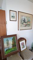 Four framed art pieces on white wall and chair showing overall lot contents and size context