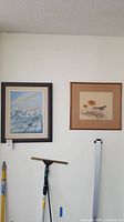 Two framed paintings hanging on the wall including a mountain landscape and a bird scene.
