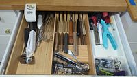 Drawer showing wooden handled cutting utensils, whisks, peelers, herb scissors, and measuring spoons organized in bamboo tray.