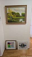 Full view of three framed artworks including large landscape painting hung on wall and two smaller framed paintings below