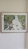Full view of the framed watercolor painting of a waterfall with rocks and trees