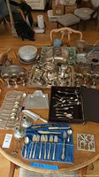 Full overview of the set on a wooden table showing various silver plated serving trays, goblets, tea set, cutlery and serving utensils.