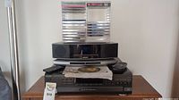 Overall shot of Bose speaker system atop Technics stereo component with stacked CDs and remotes