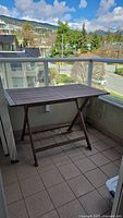 Outdoor teak folding table on a balcony with city and mountains in background.