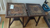 Pair of small wooden side tables with carved tops, showing square tops and three-legged stands.