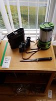Photo showing the full lot including the lantern, binoculars with case, and cutting utensil on a wooden surface.