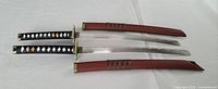 Two vintage Japanese katana swords with sheaths placed side by side on a white surface.