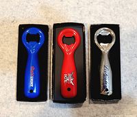 Three vintage advertising bottle openers shown side by side in individual black boxes, blue Coors Light, red Smirnoff Ice, and silver Labatt.