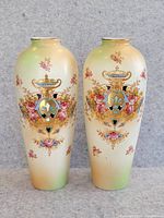 Front view of two tall antique Victorian vases with floral and urn motifs.