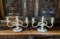 Pair of vintage silver tone 3-arm candle sticks on wooden furniture.