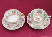 Pair of vintage teacups and saucers showing the two different patterns and sizes on a red cloth background.